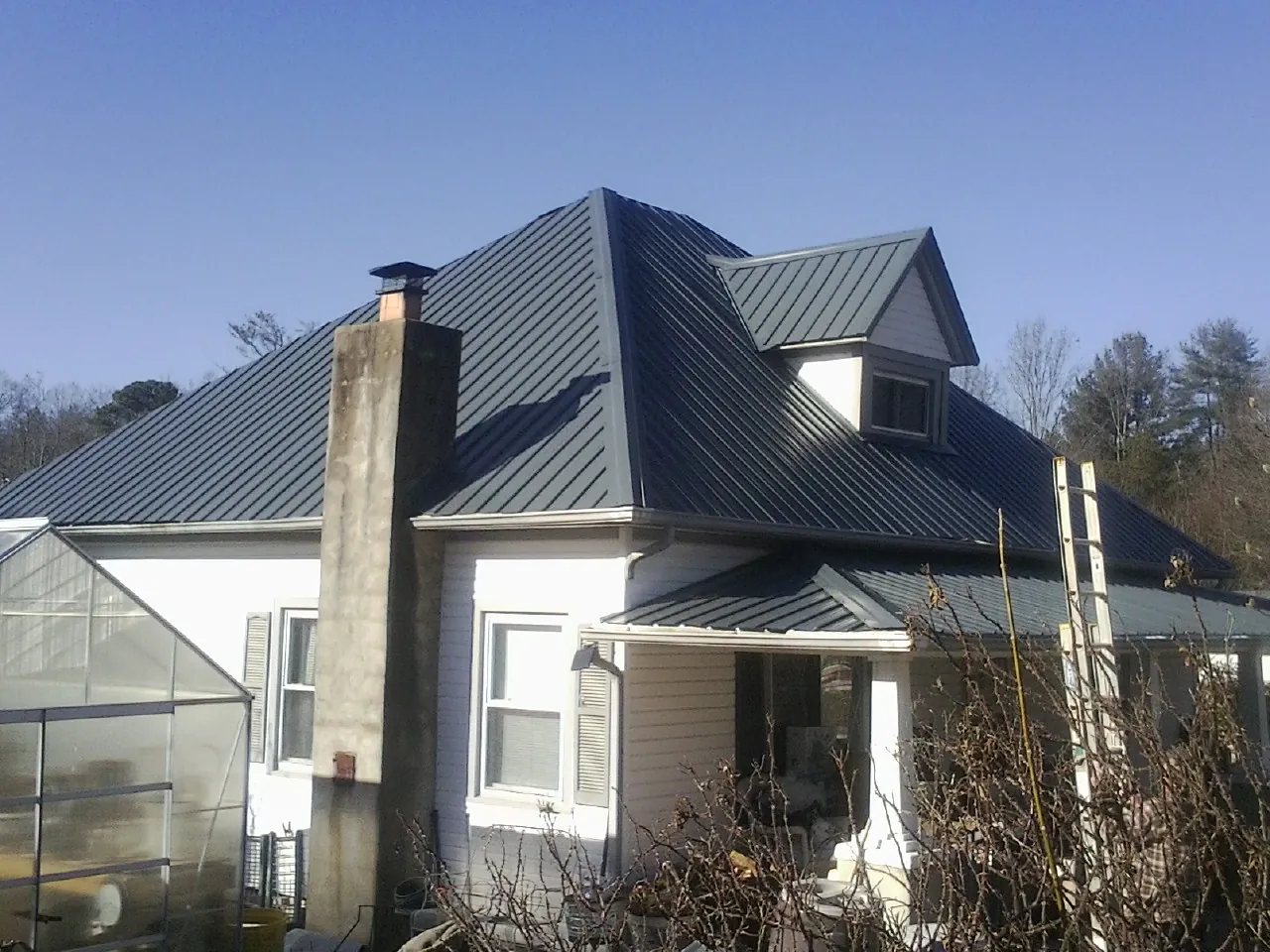 Dark blue standing seam metal roof on a white farmhouse with dormer — Slate & Tile Roof Repair by Roofing Brothers in Neptune Beach