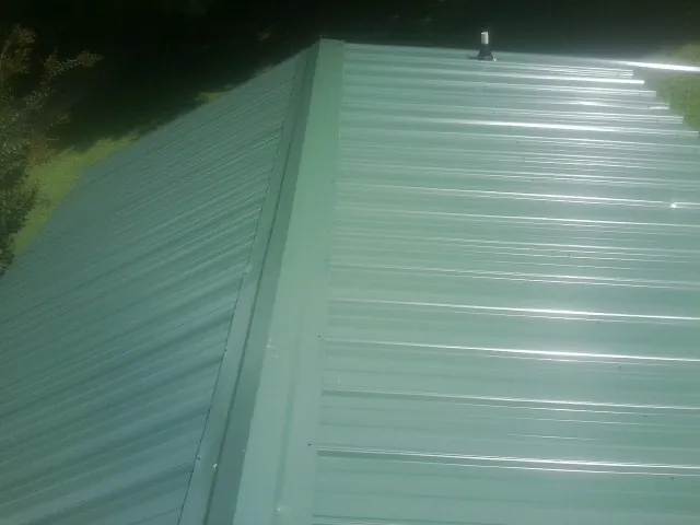 New green metal panels meeting at the ridge of a roof — Flat Roof Repair work by our crew in Neptune Beach