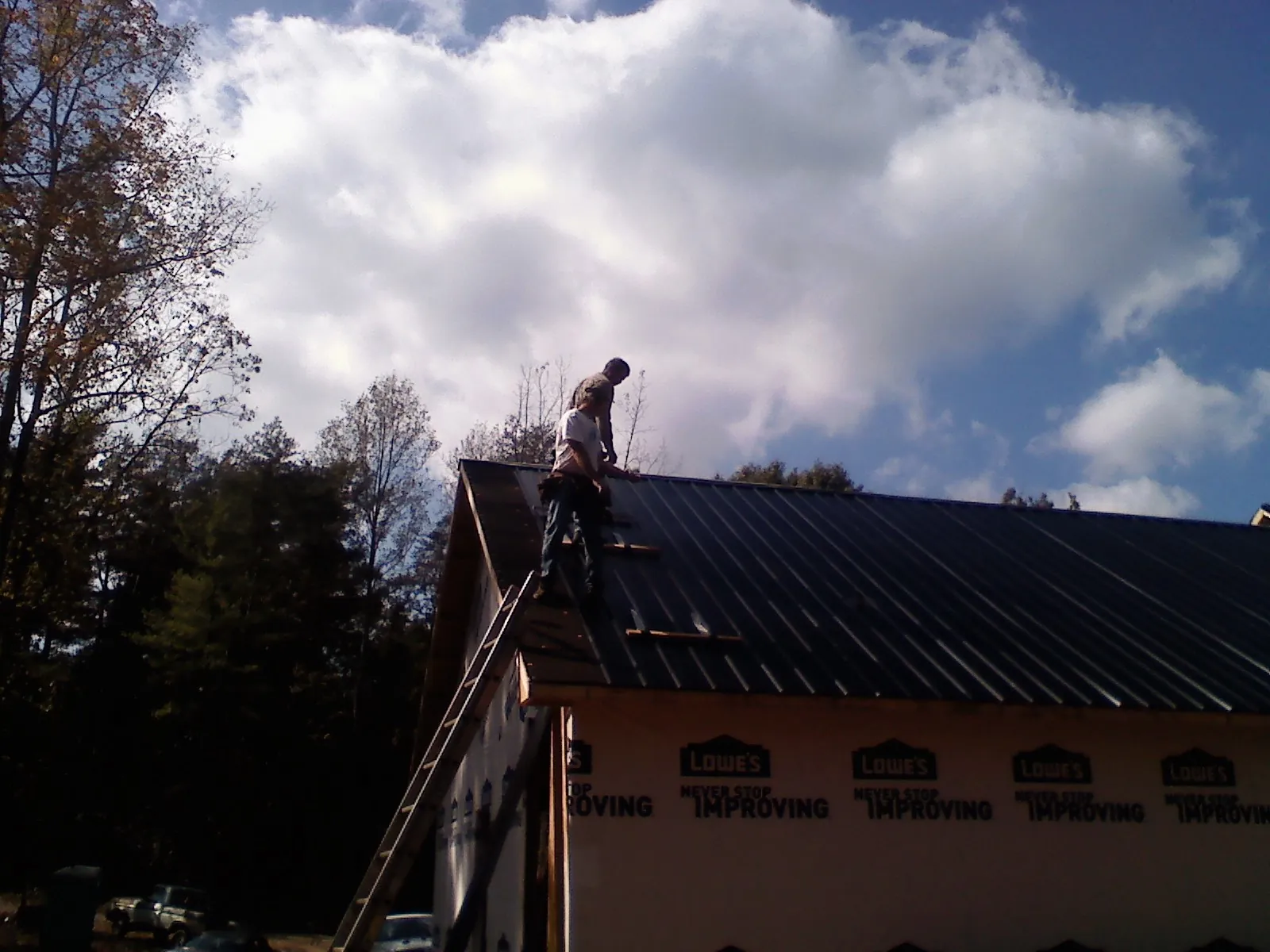 Roofer fastening dark metal panels high against a cloudy sky, from a Roof Inspection job in Neptune Beach