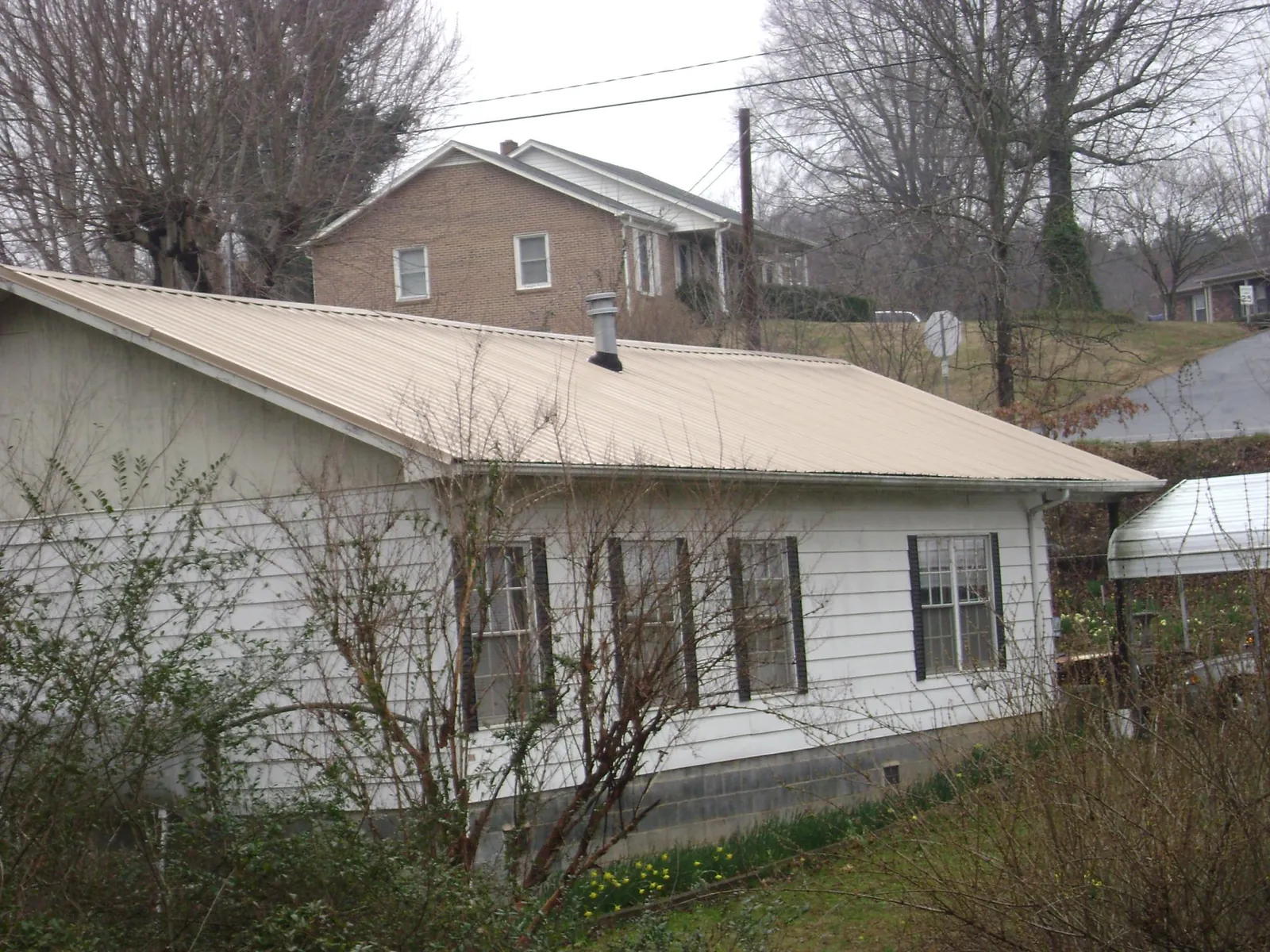 Tan metal roof on a white sided house set into a hillside — Commercial Roofing by Roofing Brothers in Neptune Beach
