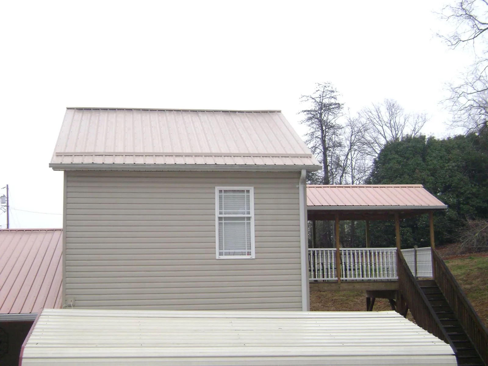 Tan metal roofs on a two story addition and attached porch, from a Roof Replacement job in Neptune Beach